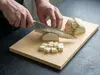 Suncraft Senzo Universal, 33-warstwowy nóż Gyuto z rękojeścią europejską, krojący warzywa na desce kuchennej.